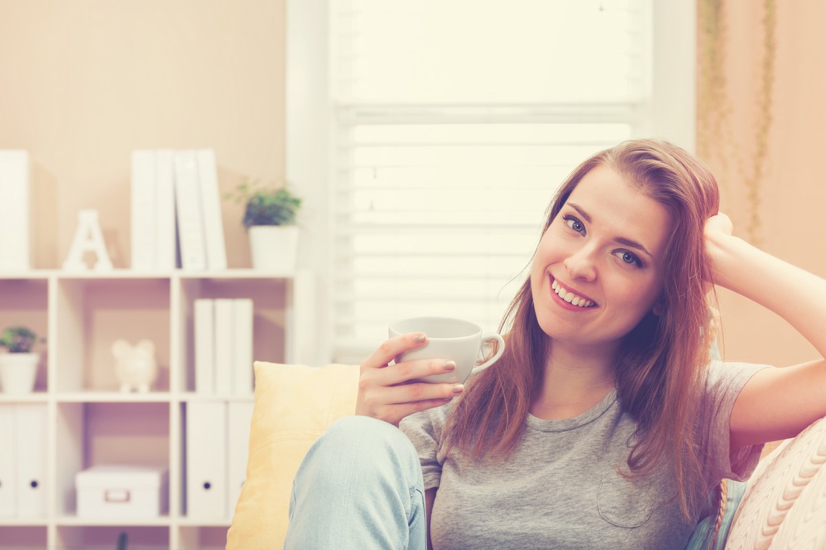 happy-young-woman-drinking-tea-on-her-couch-at-home